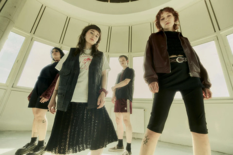 Low-angle shot of four people standing in a bright, circular room with large windows, looking down at the camera.